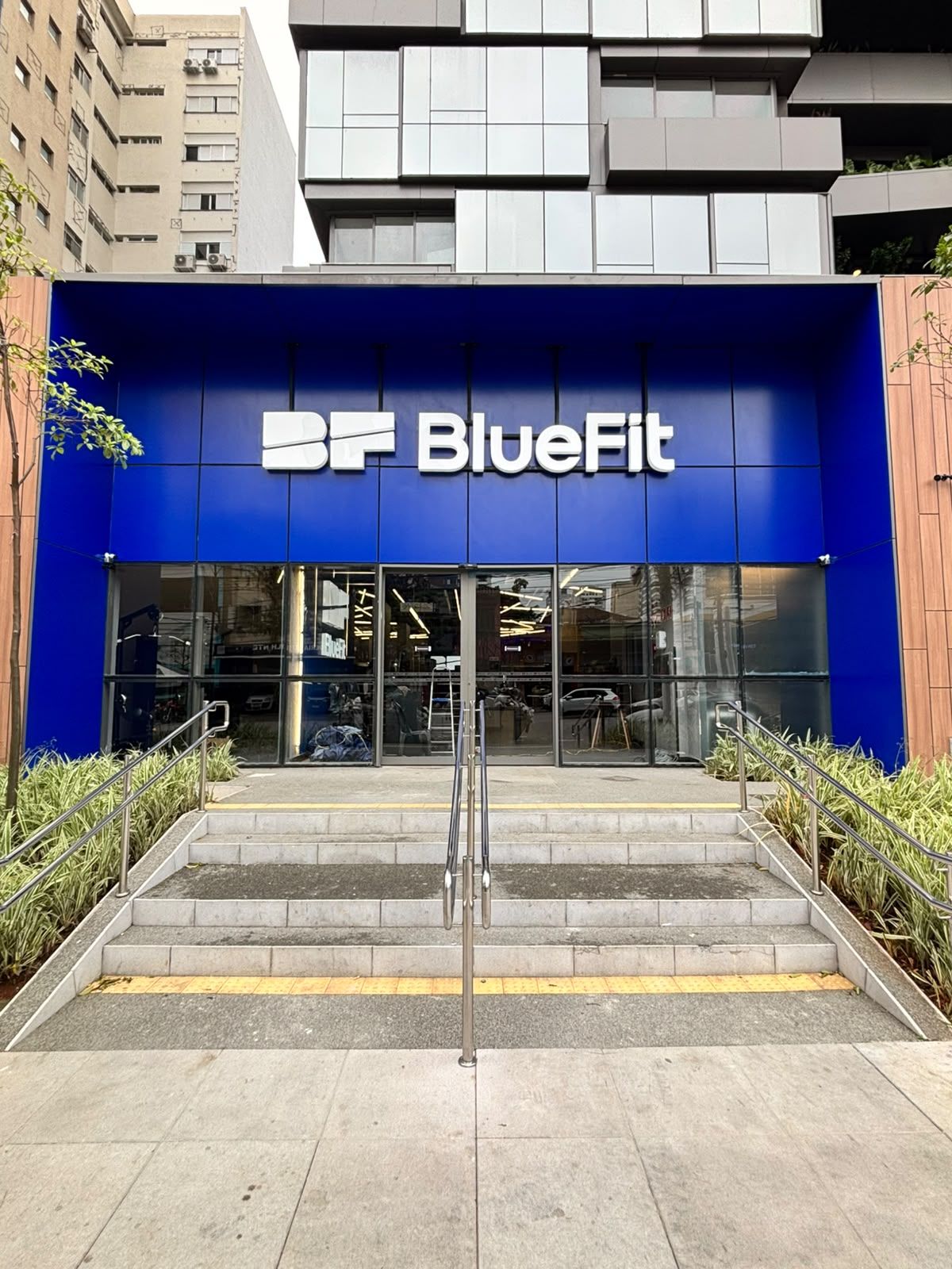 Fachada da Bluefit Pedroso de Moraes, com painel azul, letreiro da marca, porta de vidro e escada de acesso com corrimãos.